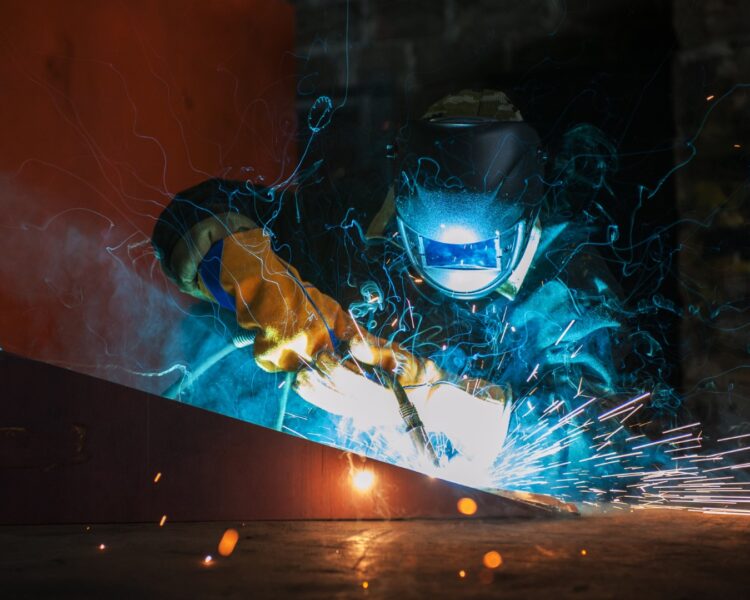 worker welding metal with sparks at factory